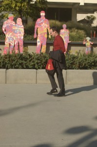 20 something man in red walks by statues going to subway