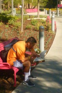 young man in ornage shirt eat a slice pf pizza while on a bench in Grand Park in downtown LA