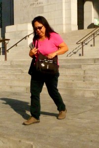 female city employee leaves city hall in pink blouse and black shoes going done the steps wile lookingher her handbag