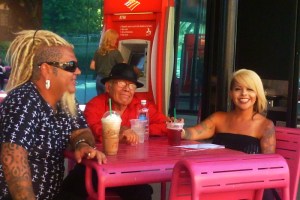 3 colorful malkes and females smile while sitting at a table in Grand Park drinbking coffee and lattes