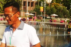 middle ages Asian man walks up step from grand Park with coffee in hand