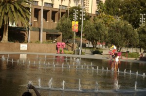 fun at Grand Park fountain, boys and girls cool off in water while teen does a trick with is skate board
