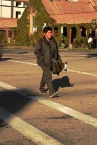 hispanic young male carries a skateboard while crossing street