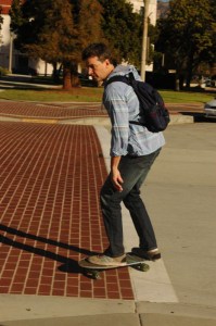 twenty something male rides a skateboard with a back pack on Pasadena Ca
