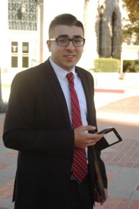 thrity something hispance amercian male ion a suit and tie, holds his I phone with phioto