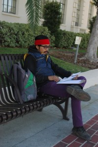 young hispanic male sits on bench outside city hall Pasadena Ca studying