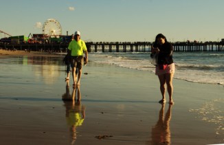 man walks close to water line =of Pacific Ocane, Santa Monica CA in ellow shirt