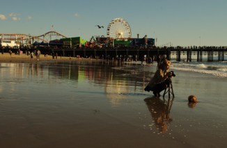female photographer with cmaera on tripod at waits ofr right wave to come in, Santa Moinca pier in background