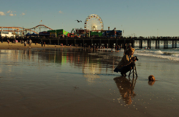 female photographer with cmaera on tripod at waits ofr right wave to come in, Santa Moinca pier in background