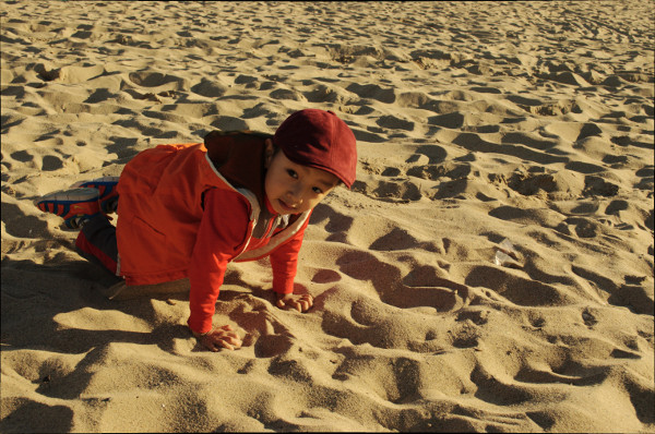 young boy in sand with red hat and matching coat, having fun