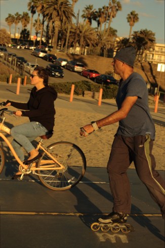 man roller blades, while a woman rides yellow bike at Santa Monica beach Nov 15