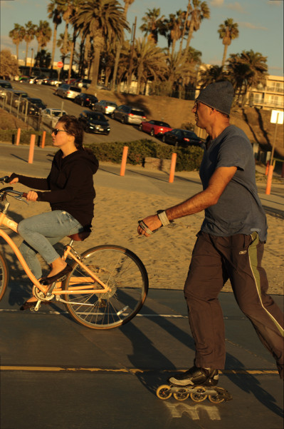 man roller blades, while a woman rides yellow bike at Santa Monica beach Nov 15