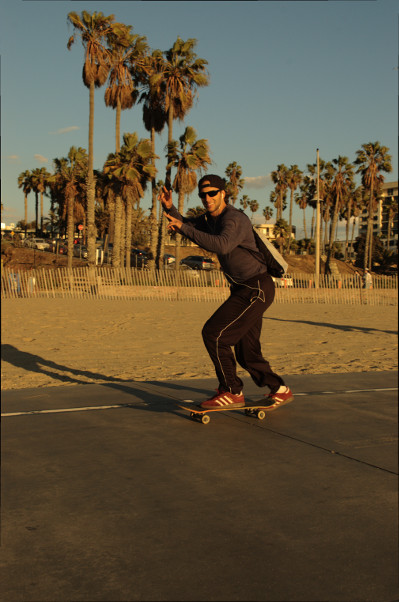 twenty somehting male waves as he rides skatebord Sonat Monica CA Nov 2014