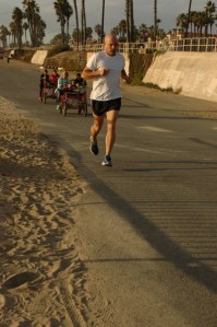 man runs at the beach while others follow in bike catrs