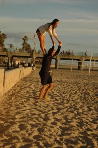 young girl luaghinly stands on mans shoulders at the beach