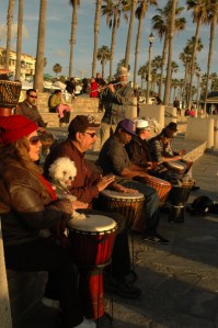 guy plays the flute while others & dog play drums at the beach