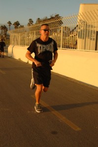 man in black exercise clothes runs at beach with sunglasses on