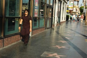 young man in all black with sunglasses stroll down Hollywood Bvld