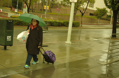 older woman walks down Hill St, Los Angeles ,CA in the rain 4/8/26