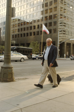 older man in business suit with case on wheels